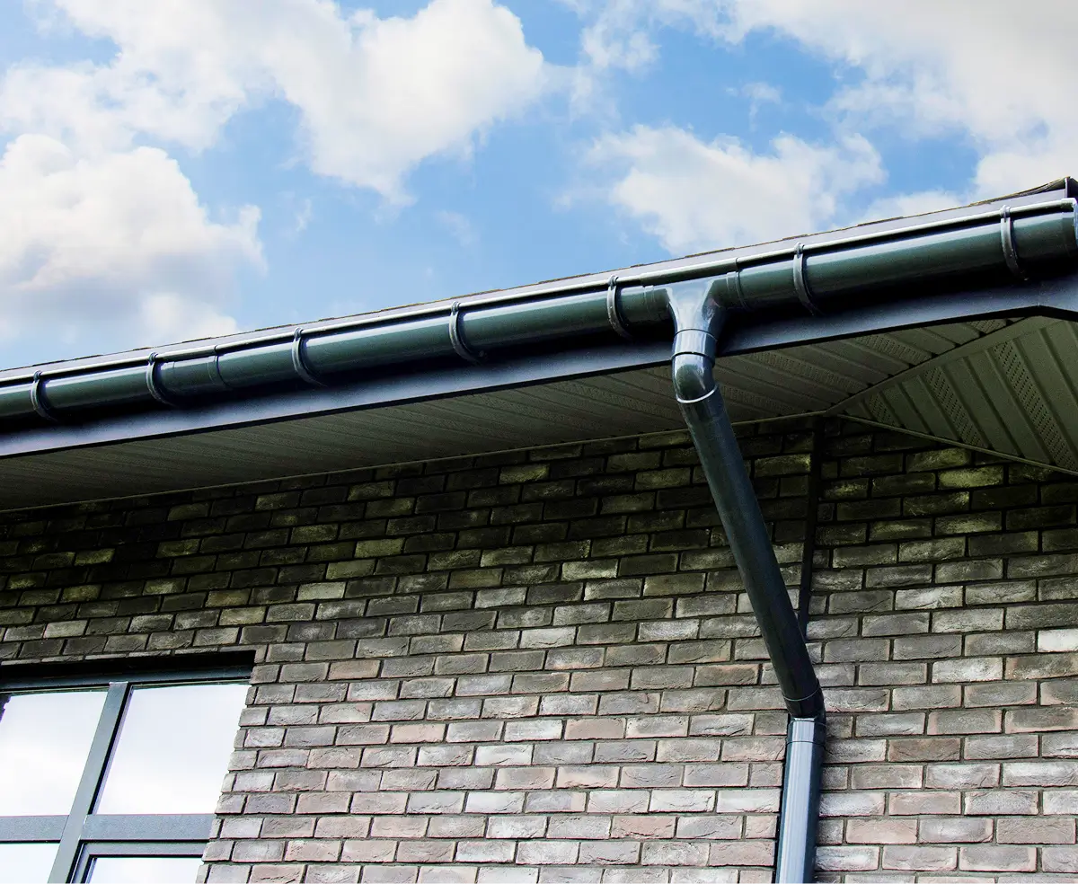 A brick wall with a window features a black gutter system under a sloped roof. The sky is partly cloudy, creating a calm, modern ambiance.